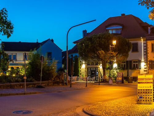 Nachtaufnahme eines Deidesheimer Cafés mit kleinem Platz, Brunnen und Stühlen