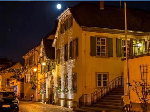 Eine beleuchtete Straße mit historischen Gebäuden und einem Vollmond über der Stadt bei Nacht. | © Forst
