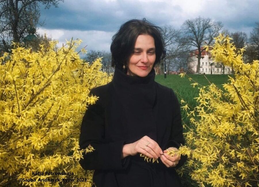 Katja Petrowskaja steht lächelnd vor blühenden, gelben Forsythien in Kyjiw, umgeben von grüner Wiese. | © Sasha Andrusyk