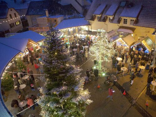 Der Weihnachtsmarkt in Meckenheim zieht viele Besucher an, während es sanft schneit und festliche Lichter leuchten.