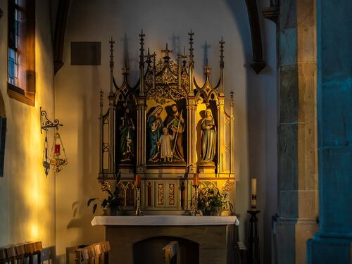 Der prächtige Altar der Ruppertsberger Kirche ist sanft beleuchtet und umgeben von Holzstühlen. | © Name