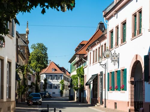 Weinstraße mit historischen Gebäuden und in Mitte Gebäude mit Beschriftung Weingut Reichsrat von Buhl