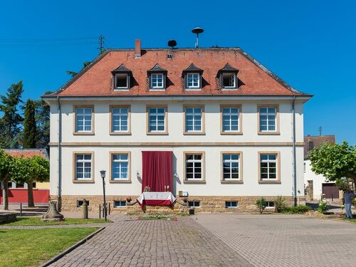 Das Gebäude in Ruppertsberg zeigt eine elegante Fassade mit roten Dächern und grünen Bäumen im Vordergrund.