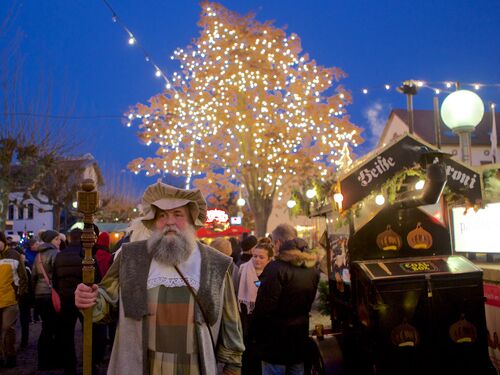 Mann im historischen Gewand des Deidesheimer Marktmeisters vor beleuchtetem Lichterbaum und Weihnachtsmarktständen