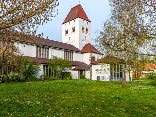 Die Kirche in Niederkirchen steht umgeben von grünem Rasen und blühenden Bäumen unter einem klaren Himmel.