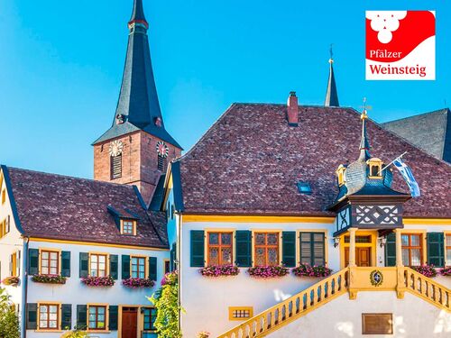 Bunte Häuser mit Blumen und Kirchturm im Hintergrund, typisch für den Pfälzer Weinsteig. | © Pfälzer Weinsteig