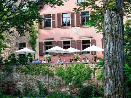 Park mit historischem Gebäude und Terrasse, auf der Menschen an Tischen essen