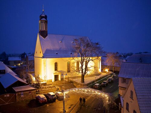 Die beleuchtete Kirche in Meckenheim strahlt im Schnee, während Spaziergänger die winterliche Nacht genießen.