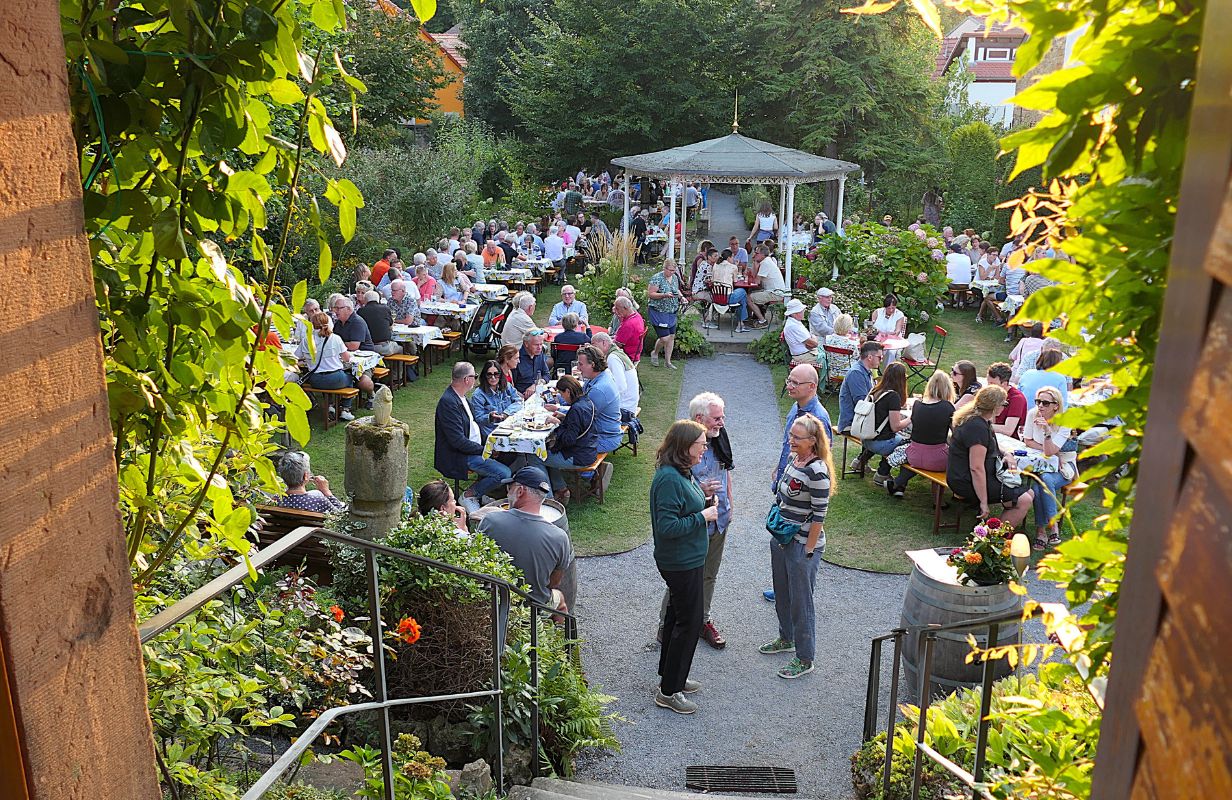 Bei der Deidesheimer Weinkerwe genießen Gäste in einem idyllischen Garten Essen und Trinken in geselliger Runde.