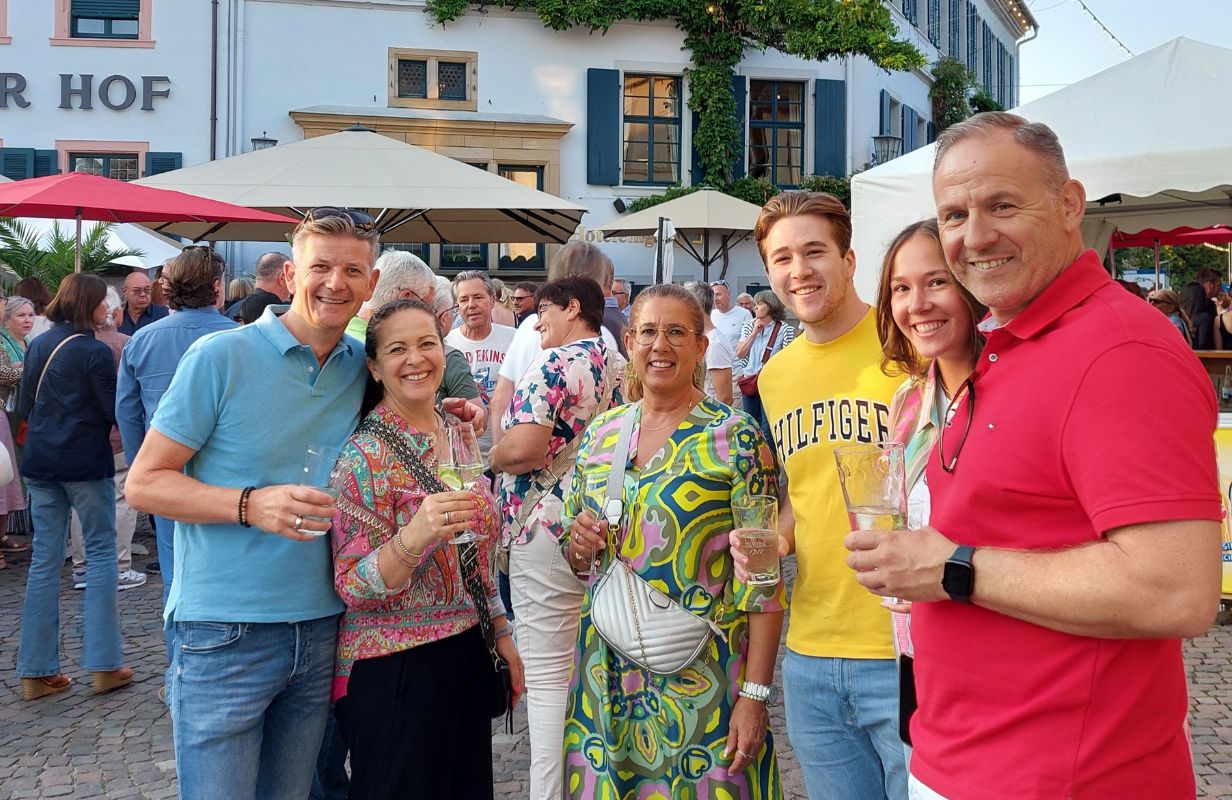 Sechs fröhliche Menschen genießen Getränke beim Deidesheimer Weinkerwe auf dem Marktplatz.